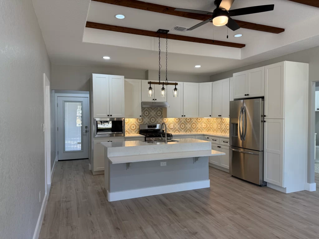 Modern kitchen featuring white cabinets, stainless steel appliances, a large island, and decorative backsplash with patterned tiles.
