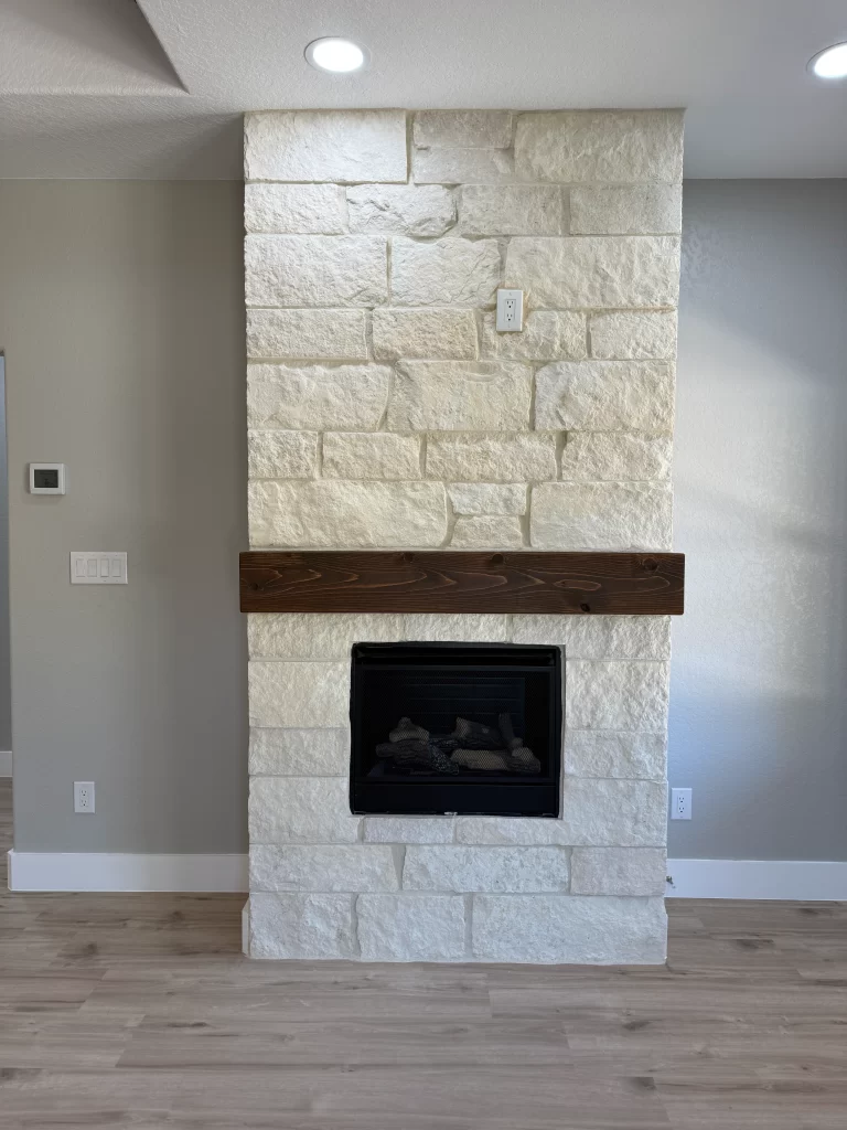 Interior view of a living room featuring a stone fireplace with a wooden mantle, light-colored walls, and recessed lighting.