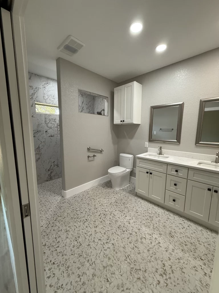 Modern bathroom featuring a double vanity with mirrors, a toilet, and a shower area, highlighted by stylish tile flooring and neutral wall colors.