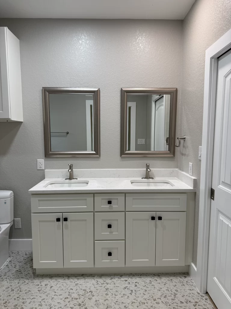 Modern bathroom with dual sinks, white cabinetry, and two framed mirrors above the sink area.