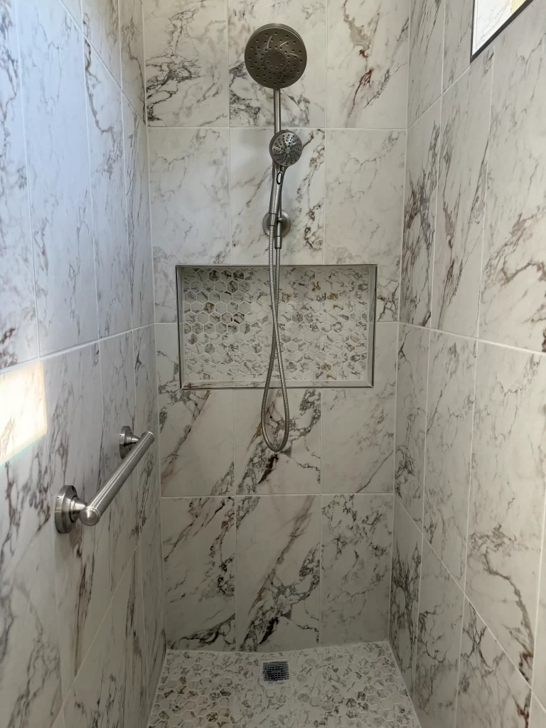 Modern shower with marble walls, a handheld showerhead, and a built-in niche for toiletries.