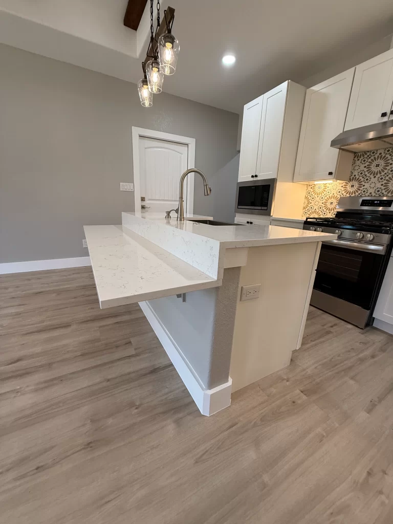 Modern kitchen featuring a white countertop with a built-in table extension, light wood flooring, and stylish pendant lighting.