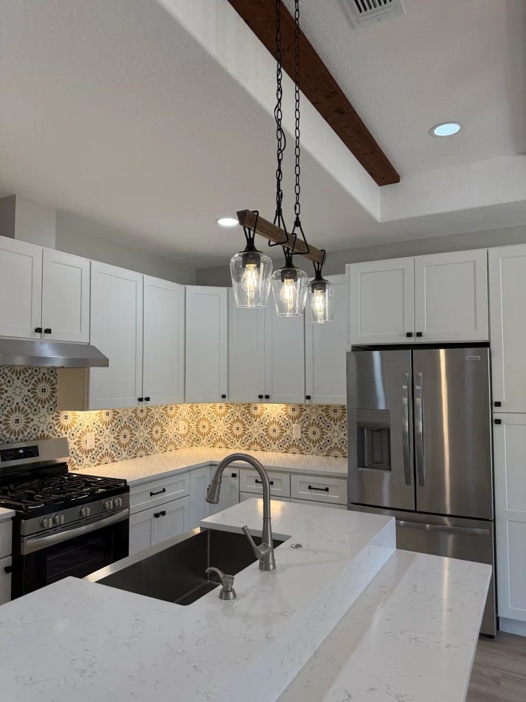 Modern kitchen featuring white cabinets, a large island with a sink, a stainless steel refrigerator, and patterned backsplash