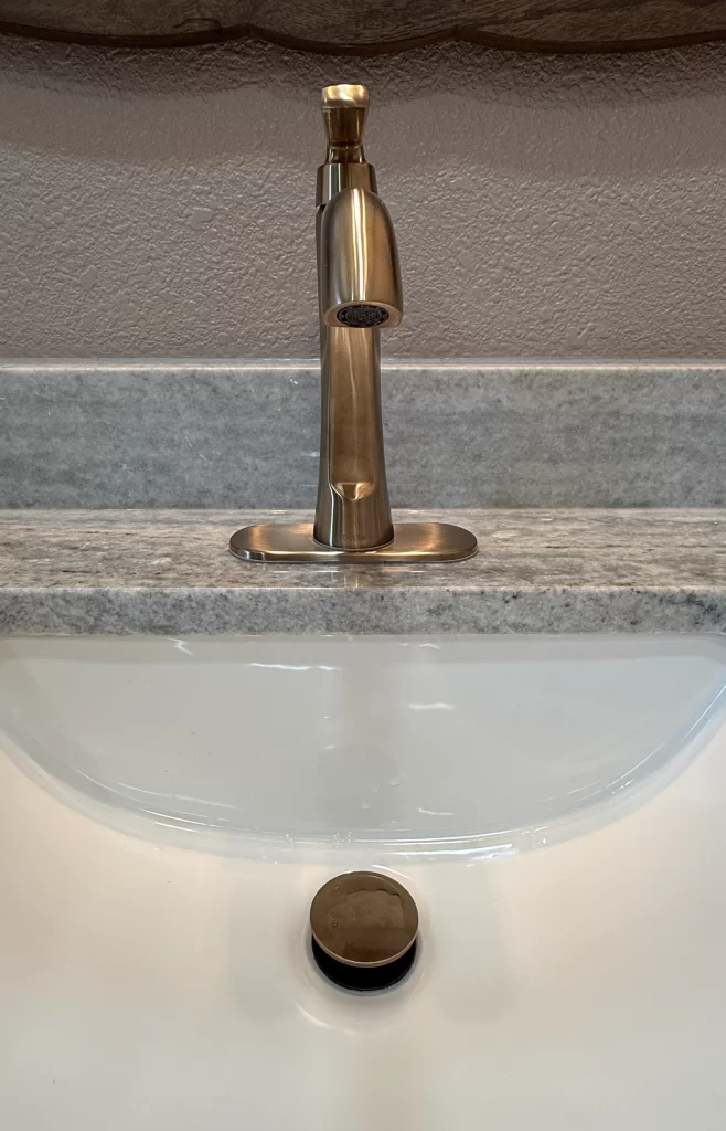 Modern bathroom faucet above white sink with a stone countertop and drain cover.
