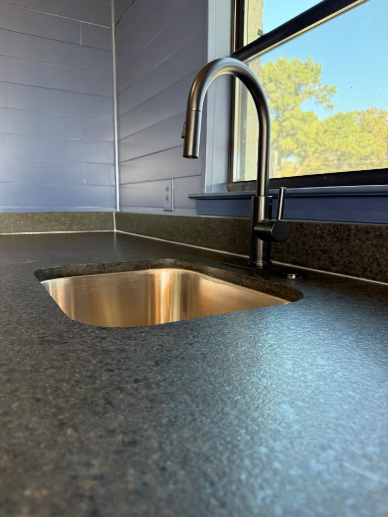 Close-up view of a modern kitchen sink with a sleek faucet, set against a light blue wall and countertop.