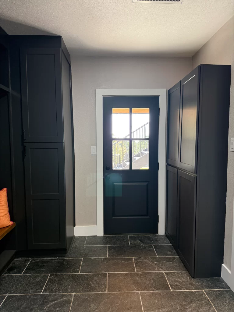 Interior view of a hallway featuring black cabinetry, a dark door with window panes, and a stone floor.