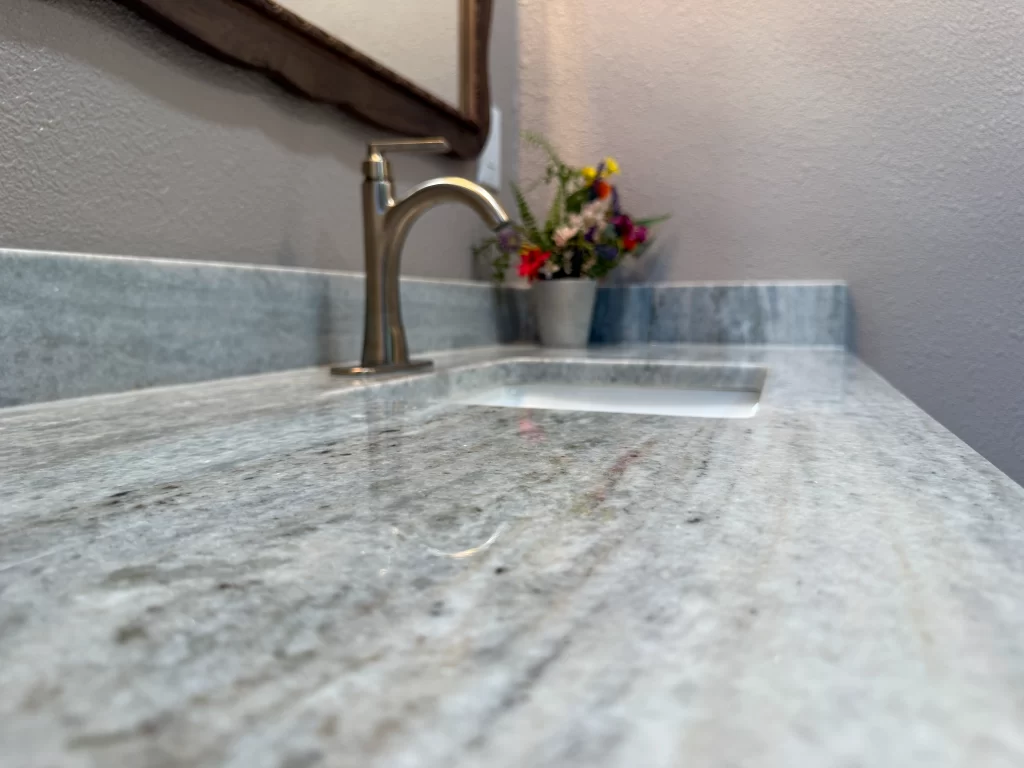Close-up of a sleek marble countertop with a modern faucet and a small potted plant with colorful flowers in the background.