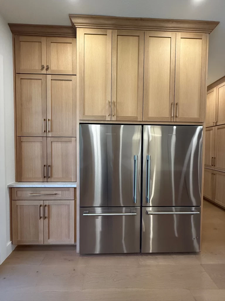 Modern kitchen featuring a stainless steel refrigerator integrated with light wood cabinetry and a marble countertop.