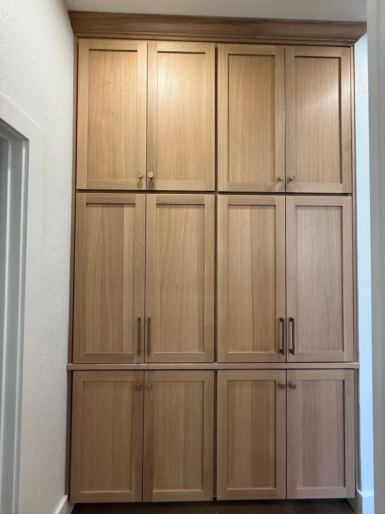 A tall wooden cabinet with multiple doors, showcasing a light wood finish and simple handles, positioned against a white wall.