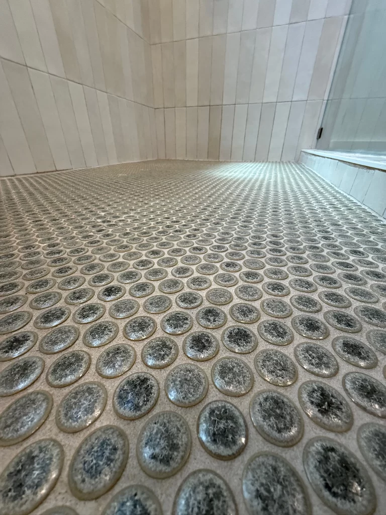 Close-up view of a textured shower floor with oval-shaped tiles, surrounded by light-colored tiled walls.