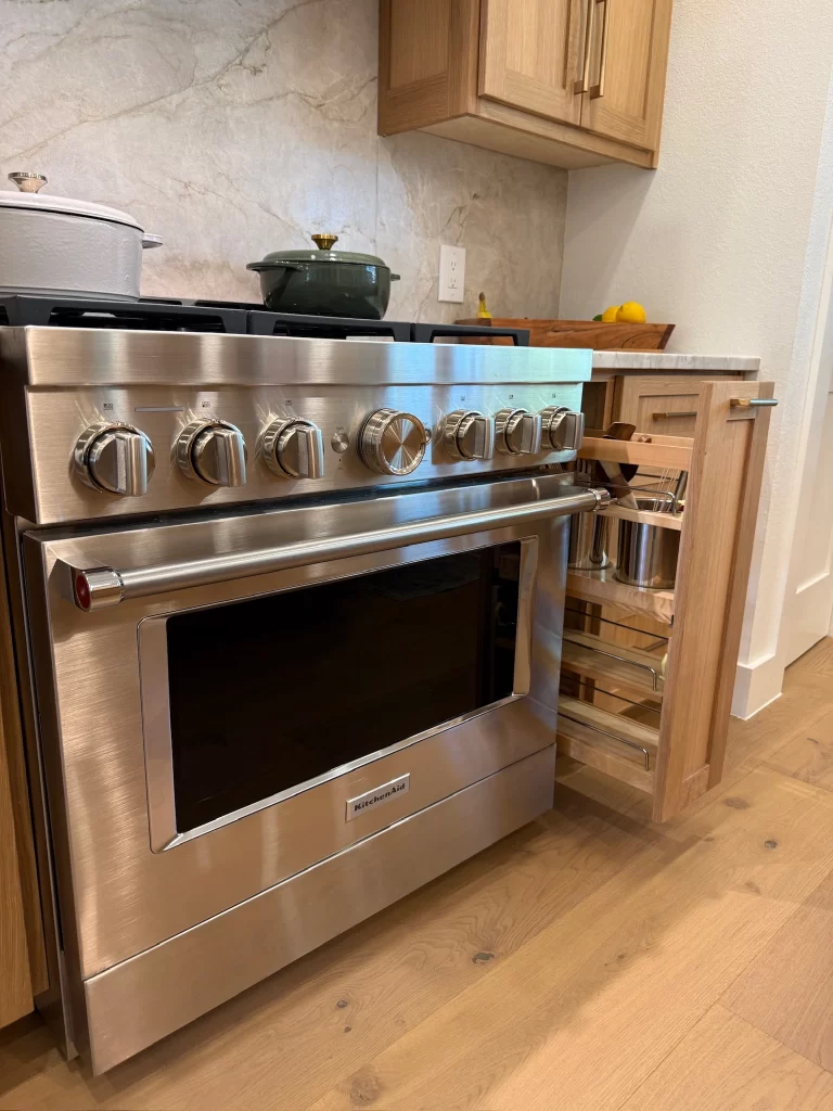 A modern stainless steel kitchen stove with a built-in oven, featuring multiple knobs, and a drawer partially open next to it, set in a contemporary kitchen with wooden cabinetry.