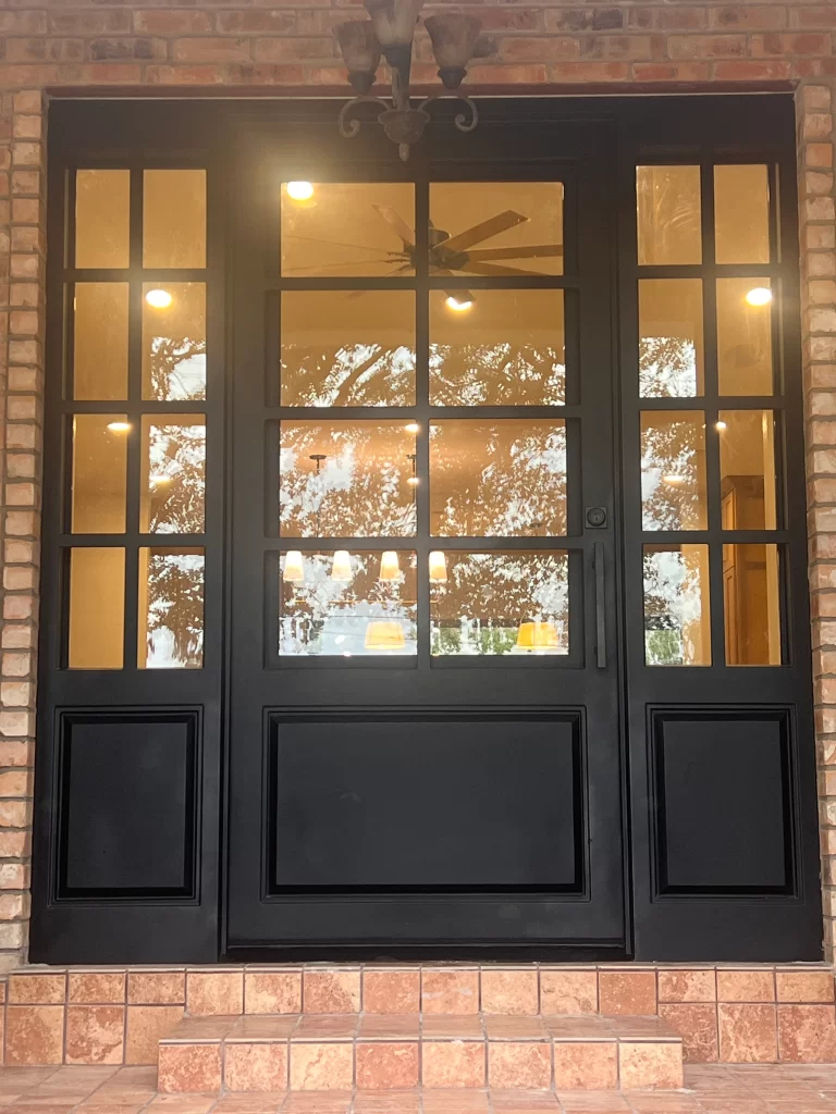A modern black front door with glass panels, set against a brick wall and a tiled entryway.