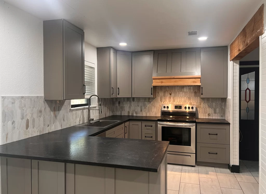 Modern kitchen featuring gray cabinets, a black countertop, and stainless steel appliances, with a stylish tile backsplash.